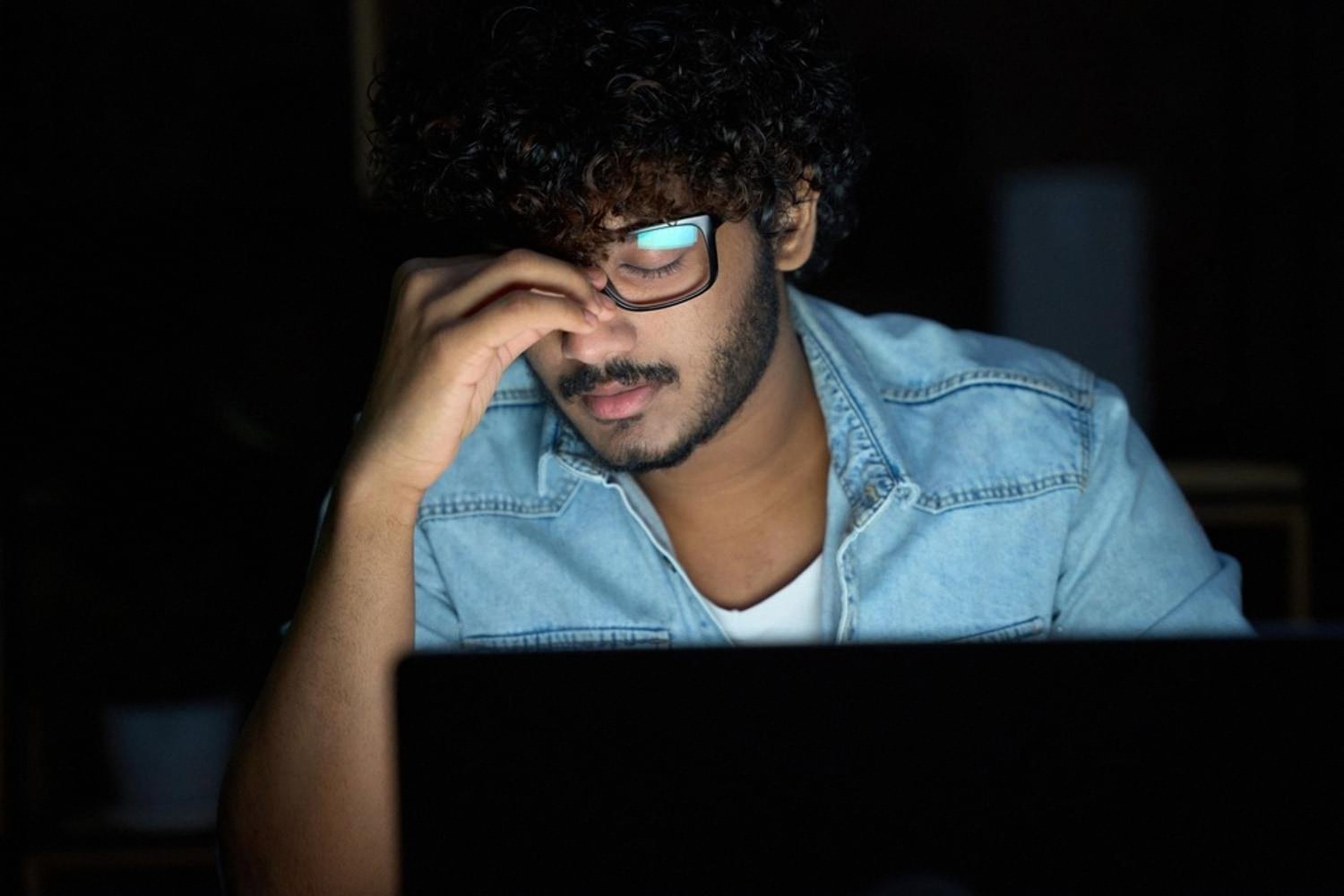 Tired young man in front of a laptop late at night, stressed about money
